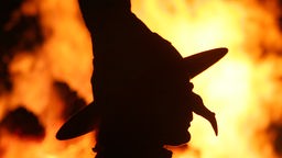 Eine als Hexe verkleidete Person im Gegenlicht eines Maifeuers