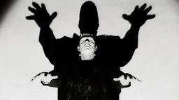 Frankenstein's Monster hebt bedrohlich die Arme, sein Schatten lässt ihn noch größer wirken.