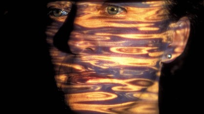 Projektion von Wellen auf dem Gesicht einer traurig schauenden jungen Frau mit grünen Augen.