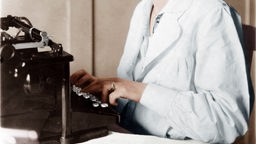 Zu sehen ist der Oberkörper einer Frau, welche auf einer Schreibmaschine tippt.