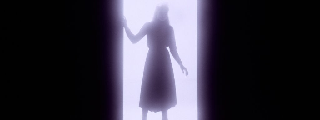 In einem Tührrahmen ist das Schema einer Frau zu erkennen, ihr Schatten fällt auf den Boden.