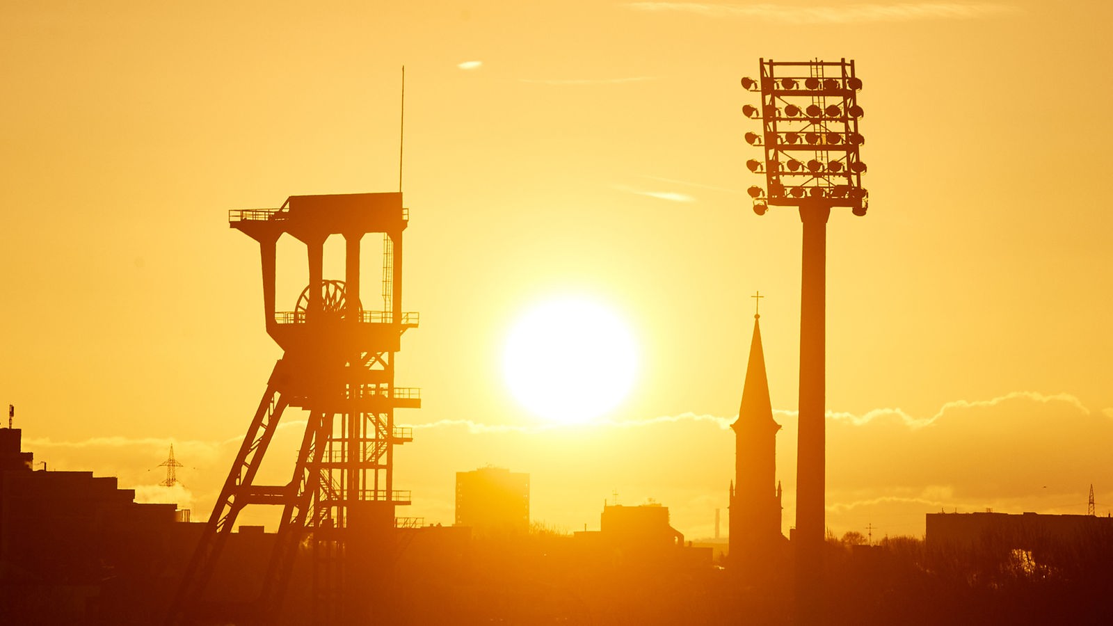 Die Sonne geht über dem Förderturm der Zeche Holland und einem Flutlichtmast des Lohrheidestadion in Bochum auf.