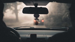 Innenansicht eines Autos, Bremslichter eines anderen Autos sind durch die Frontscheibe ominös zu beobachten.