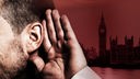 Ein Mann hält seine Hand an sein Ohr, hinter ihm ist das Parlamentsgebäude in London zu sehen.