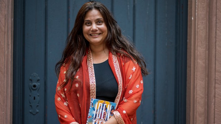 Autorin Mithu Sanyal hält lächelnd ihr Buch "Identittti" in der Hand.