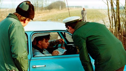 Zwei Polizisten kontrollieren den Reisepass eines Mitfahrers in einem Auto.