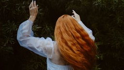 Rückenansicht einer tanzenden Frau mit langen roten Haaren in weißem Kleid.