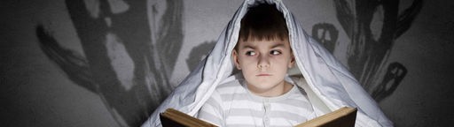 Ein Junge liest unter einer Decke Gruselgeschichten. 