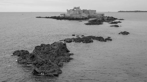 Schwarz-Weiß: Gezeiten-Insel Petit-Bé mit Fort National, umgeben von Felsen im französischen Meer.