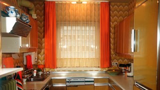 Ein Fenster mit orangenen Vorhängen in einer Küche aus den siebziger Jahren.