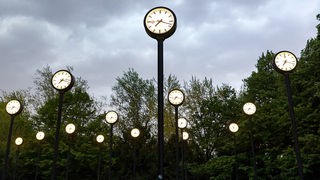 Mehrere Uhren der Installation 'Zeitfeld' von Klaus Rinke vor verdunkeltem Himmel.