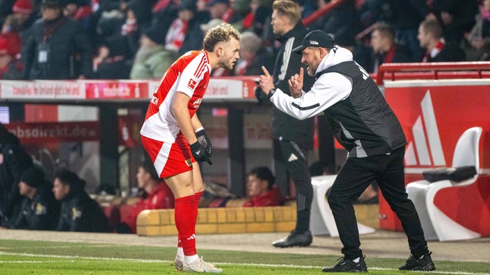 Berlins Mittelstürmer Benedict Hollerbach (links) diskutiert vor der Trainerbank mit Coach Steffen Baumgart (rechts)