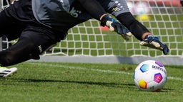 Hände eines sich werfenden Torwarts greifen nach Bundesliga-Ball (offizieller Spielball Derbystar 2023/24)