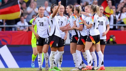 Spielerinnen der Frauen-Nationalmannschaft freuen sich auf dem Spielfel im Hintergrund Publikum und deutsche Flaggen