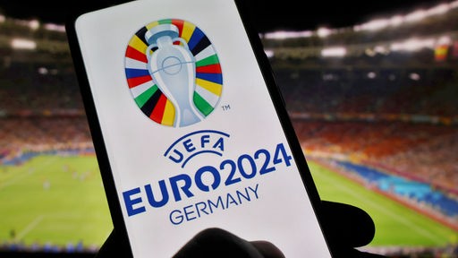 Das Logo der UEFA Euro 2024 ist auf einem Smartphone vor Stadionkulisse zu sehen