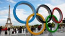 Olympische Spiele Paris 2024: große Olympische Ringe auf Platz mit Passanten - im Hintergrund der Eiffelturm