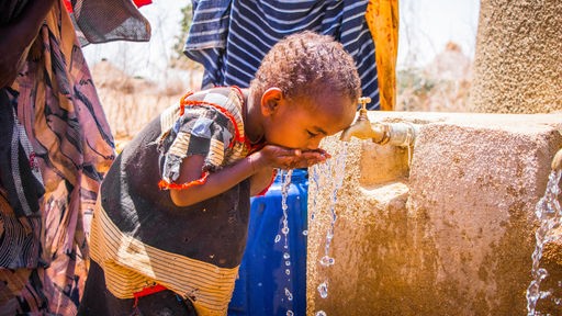 Ein Junge trinkt Wasser aus einem Trinkbrunnen, der von dem Hilfsprojekt Arche NoVa gebaut wurde