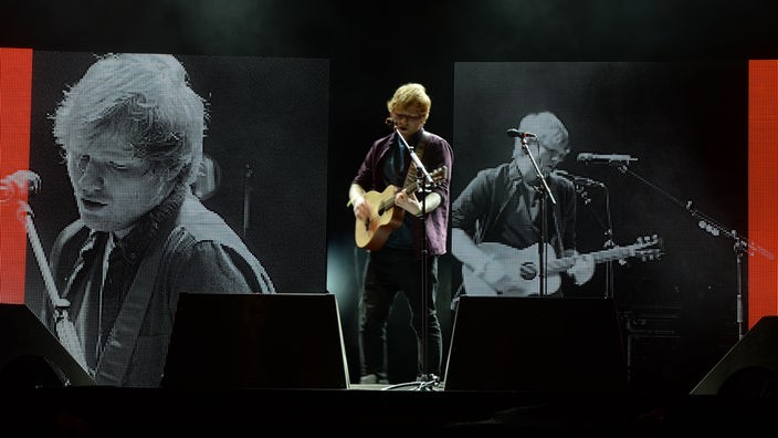 Ed Sheeran steht auf der Bühne mit Gitarre in der Hand hinter dem Mikrofon