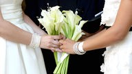 Die Hände zweier Bräute in Weiß bei der Hochzeitszeremonie