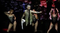 Robbie Williams singt, wären drei Tänzerinnen ausdrucksvoll posieren