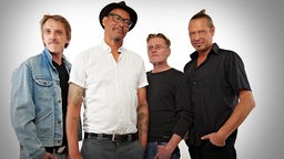 Die vier Bandmitglieder posieren vor einem hellen Hintergrund.