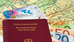 Reisepass, Krankenversicherungskarte und Euros liegen auf einer Landkarte