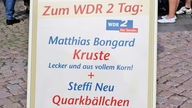 Werbeaufsteller einer Bäckerei: "Matthias Bongard Kruste" und "Steffi Neu Quarksbällchen"