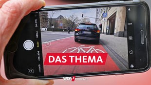 Auf einem Smartphone ist das Bild eines Autos zu sehen, das auf einem Radfahrstreifen hält.