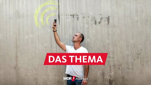 Symbolbild Funkloch: Mann steht mit erhobenem Smartphone vor einer Betonwand, auf die ein WiFi-Zeichen mit Kreide aufgemalt ist