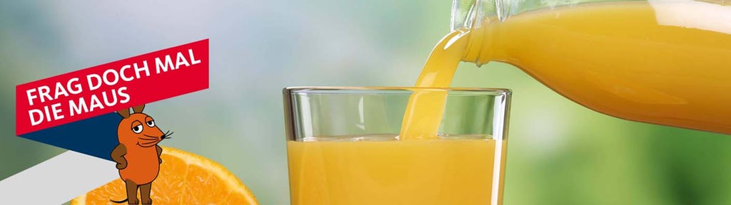 Aus einer Karaffe wird Orangensaft in ein Glas gegossen, daneben eine aufgeschnittene Orange