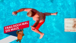 Ein Junge springt in einem Freibad vom Sprungbrett ins Wasser. 