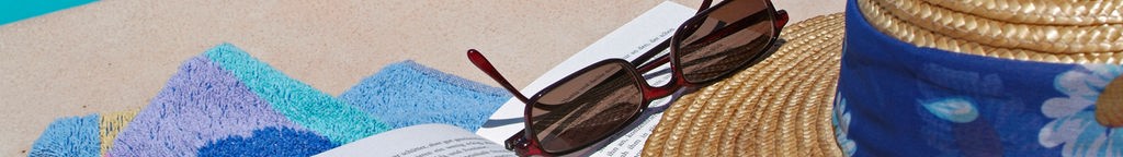 Ein aufgeschlagenes Buch, Sonnenbrille und Strohhut liegen an einem Pool