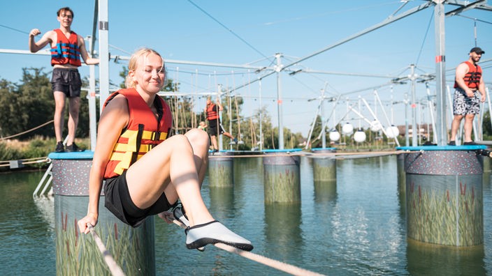 Aqua-Climb in Selm: Eine junge Frau sitzt auf zwei Seilen über dem Wasser