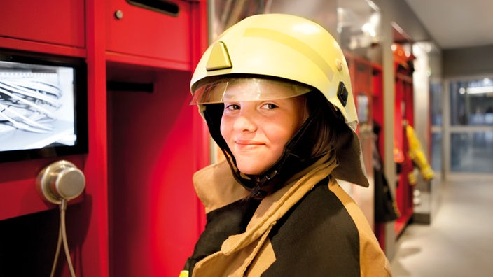 Ein Kind trägt eine Feuerwehruniform und lächelt in die Kamera