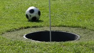 Fußball liegt auf einer Fußballgolfanlage neben einem Loch