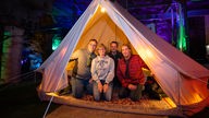 Steffie, Marcus, Ralph und Michi knien im WDR 2 Zelt im Besucherbergwerk Ramsbeck und lächeln in die Kamera