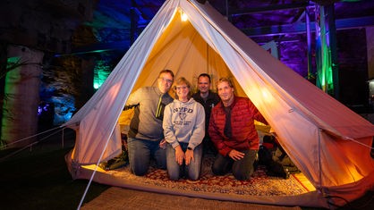 Steffie, Marcus, Ralph und Michi knien im WDR 2 Zelt im Besucherbergwerk Ramsbeck und lächeln in die Kamera