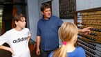 Stephan Stamen führt seinen Kindern Mathis und Johanna in der alten Landschule auf dem Mühlenhof in Münster einen Rechenschieber vor
