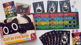 Die Schachtel von "Cat in the Box" zeigt eine schwarze Katze, daneben schwarze Spielkarten mit Katzenmotiven und ein vierfarbiges Spielbrett, auf dem bunte Spielsteine liegen
