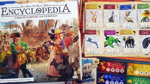 Die Spieleschachtel von "Encyclopedia" neben dem farbenfrohen Spielplan, auf dem Karten mit bunten Tierillustrationen und Würfel liegen