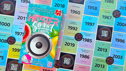 Die bunte Spieleschachtel von "Hitster" liegt auf einer Anordnung farbiger Songkarten, die jeweils Name, Interpret und Erscheinungsjahr eines bekannten Songs zeigen