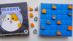 Die Spieleschachte von "maunz." zeigt eine fröhliche Comic-Katze, daneben Katzenspielsteine auf einem dreidimensionalen "Spielbett" von 6 mal 6 Feldern
