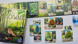 Die Spieleschachtel von "Mischwald", daneben eine Kartenauslage, bei der verschiedene Tierkarten seitlich hinter Baumkarten hervorschauen