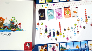 Die weiße Spieleschachtel von Tokaido, daneben der Spielplan mit dem aufgemalten Weg, Spielfiguren und zahlreichen bunten Karten