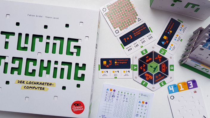 Die Spieleschachtel von Turing Machine liegt neben dem Spielmaterial, das aus Lochkarten, Testkarten und Antwortkarten mit Häkchen und Kreuzen besteht