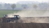 Aufgrund der Trockenheit hängen große Staubwolken über Traktoren bei der Feldarbeit