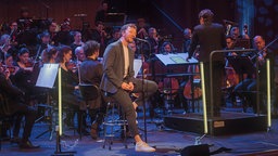 Joris mit Musiker:innen des WDR Funkhausorchesters auf der Bühne.