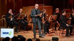 70 Jahre Musik der Zeit: Der Moderator Michael Struck-Schloen spricht auf der Bühne des Klaus-von-Bismarck-Saals vor dem WDR Sinfonieorchester