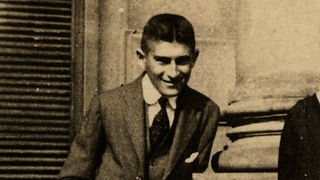 Kafka lehnt sich lächelnd an an eine Säule des Opelthauses in Prag.