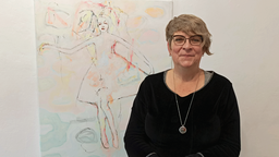 Galeristin Kirsten Adamek steht vor einem Kunstwerk von Jón Thor Gislason. Auf dem Bild sieht man eine Tänzerin.